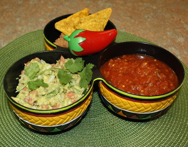 three bowls with a decorative red pepper connecting them.  One bowl contains homemade salsa, one contains my favorite yummy guacamole recipe and the other contains bean dip. happy dipping