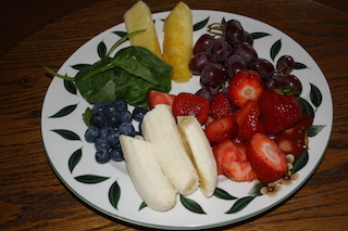 A plate with bananas, strawberries, grapes, pineapples spears and spinach--ready to be blended into a delicious smoothie to lower cholesterol and improve health