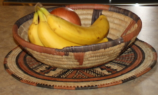 a decorative handmade African basket containing a bunch of bananas and another fruit