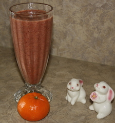 two cute bunny salt shakers by a mandarin orange smoothie and a ripe mandarin orange
