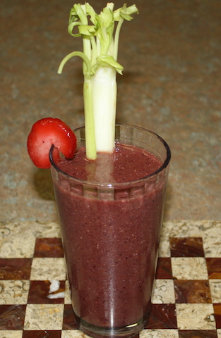 smoothie with strawberry slice on rim and rib of celery to dip into and eat
