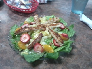 A salad containing fresh fruit and grilled chicken strips. Pretty and nutritious