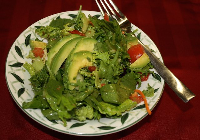 A crispy tossed salad with avocados on top, dressed and ready to enjoy