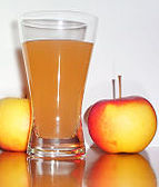 a tall glass of apple juice sitting on the table with two crispy apples. A tasty treat,