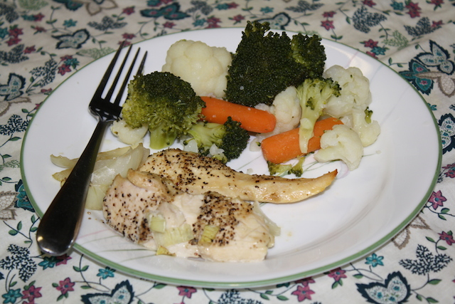 baked chicken and steamed onions, cauliflower, broccoli and carrots on a dinner plate