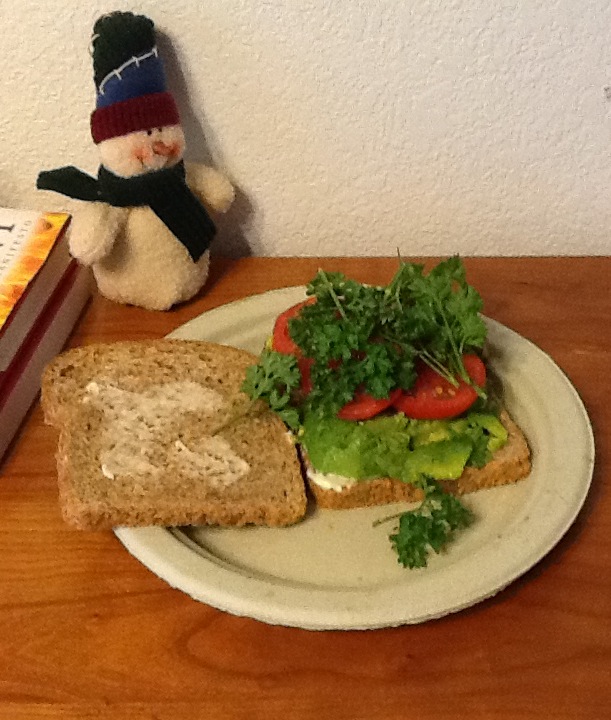 A yummy avocado sandwich with parsley and sliced tomatoes on a paper plate. A quick lunch when you are busy.