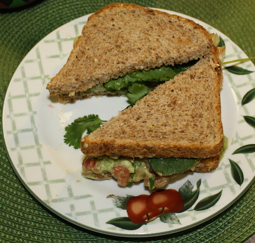 A lovely sandwich made on sprouted grain bread filled with colorful homemade guacamole