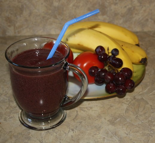 A berry colored smoothie beside a plate of fruit looks delicious