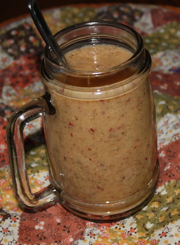 A tasty tannish smoothie with flecks of red from grapes. served in a clear glass mug. very nice for breakfast